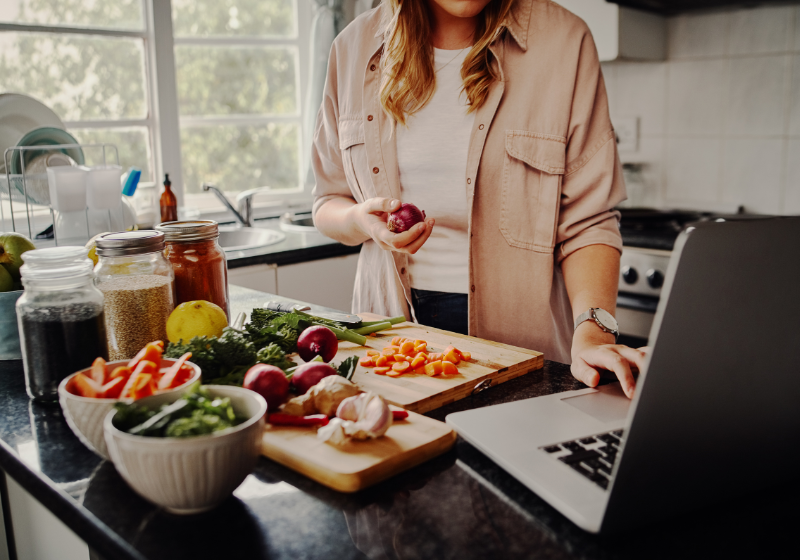 Frau kocht in der Küche und schaut nebenbei auf den Laptop