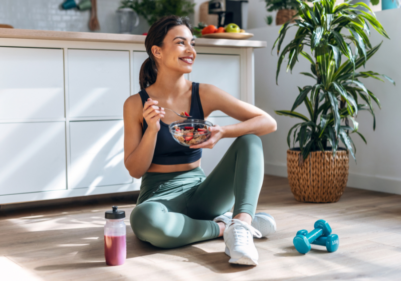 Frau auf dem Küchenboden isst Müsli und trinkt Smoothie
