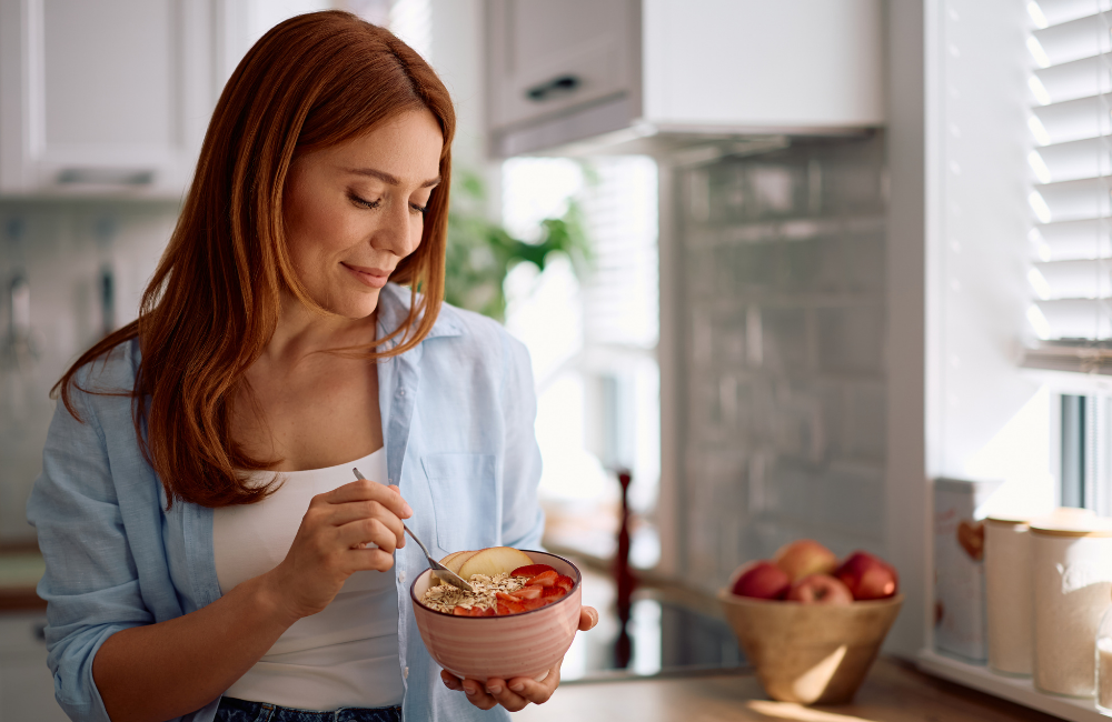 Kritische Nährstoffe bei veganer Ernährung Beitragsbild: Frau in der Küche isst Müsli mit Apfel und Erdbeeren