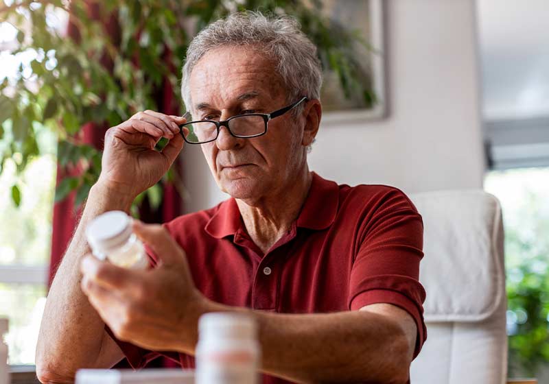 alter mann mit brille liest packungsbeilage von medikament