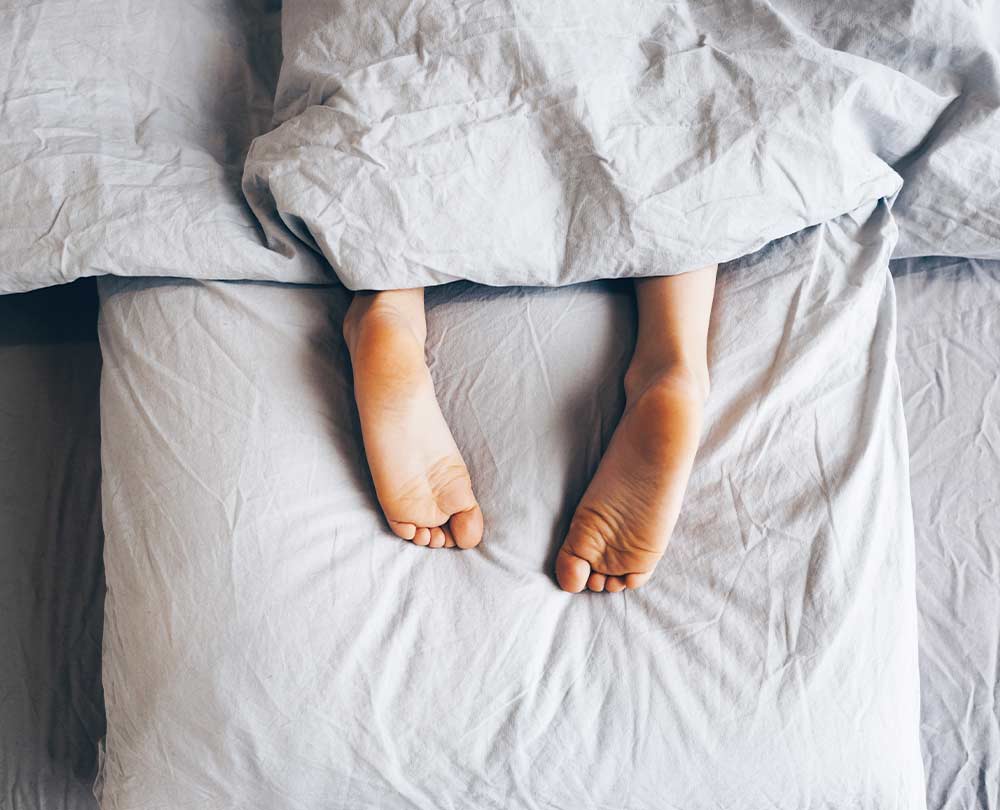 warum bin ich immer müde beitragsbild: beine schauen aus der bettdecke